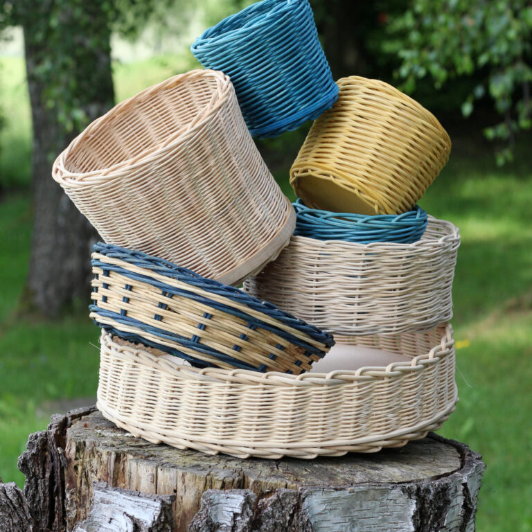 Verschiedenfarbige geflochtene Körbe, teils naturbelassen, teils bunt, sind locker auf einem Baumstumpf im Freien gestapelt.