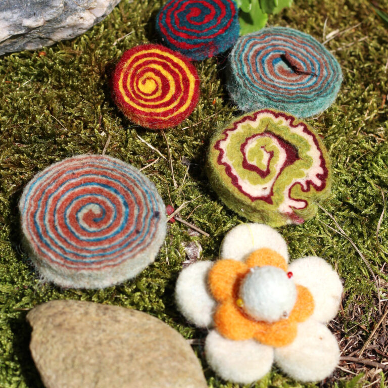 Buntes Filzkonfetti liegt auf einem mit Moos bewachsenem Stein