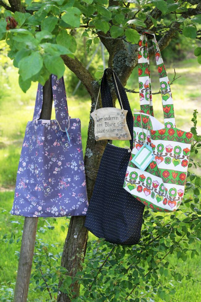 Bunte Stofftaschen hängen zusammen mit einem Keramikschild in einem Baum.