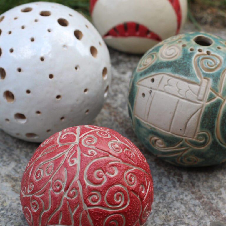 Bunt angemalte Keramikbälle liegen auf einem Stein.