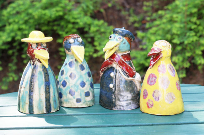 Bunte, lustige Keramik Vögel stehen auf einem Türkis angemalten Tisch im Garten.