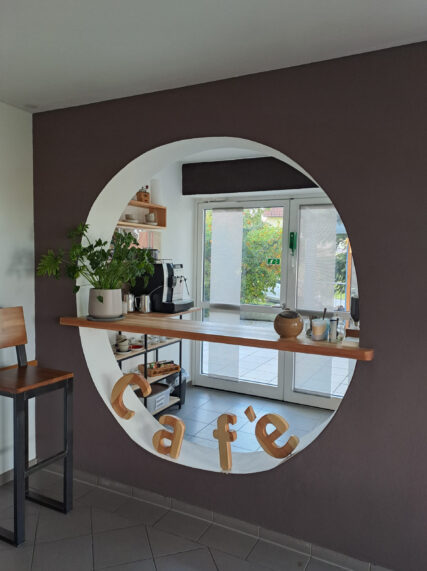 Blick auf die gesamte Kaffeebar mit Kaffeemaschine, Holzbuchstaben und einer Pflanze.