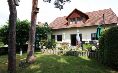 Gepflegter Garten hinter dem Haus mit Terrasse, Gartenmöbeln und Sonnenschirmen – umgeben von Bäumen und Hecken.